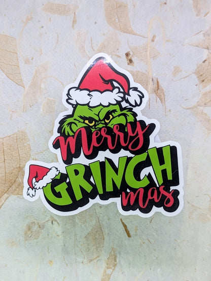 Sticker with Grinch design and 'Merry Grinchmas' text on a textured surface